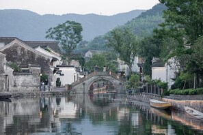 A traditional Chinese water town with a stone bridge over a canal, surrounded by lush greenery and historic buildings. - Blossom Hill Hotel Ningbo Hanling (Ningbo)