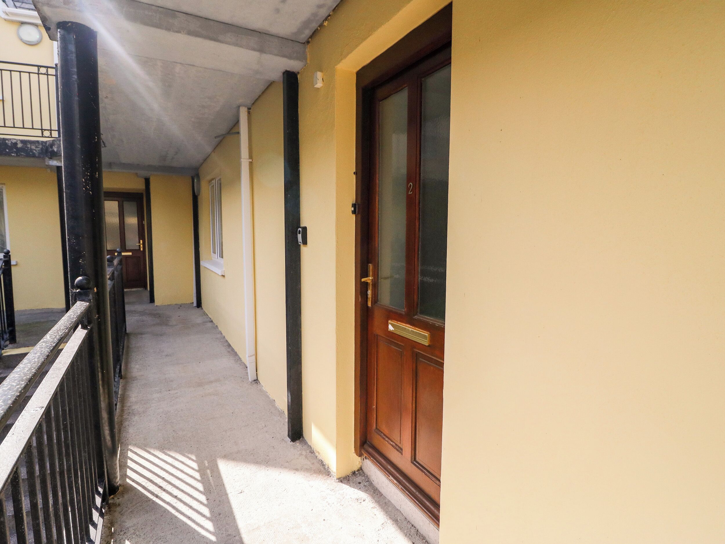 Un pasillo con una puerta de madera, una ventana y una barandilla de metal negro.