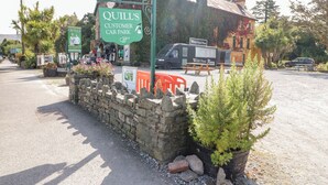A stone wall with a sign for Quill's Customer Car Park, a food truck, and a building with a tiled roof. - 2 Garnish Court (Glengarriff)