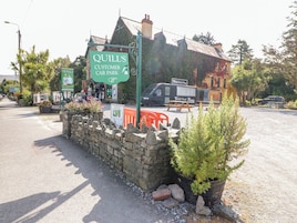 A stone wall with a sign for Quill's Customer Car Park, a food truck, and a building with a tiled roof.