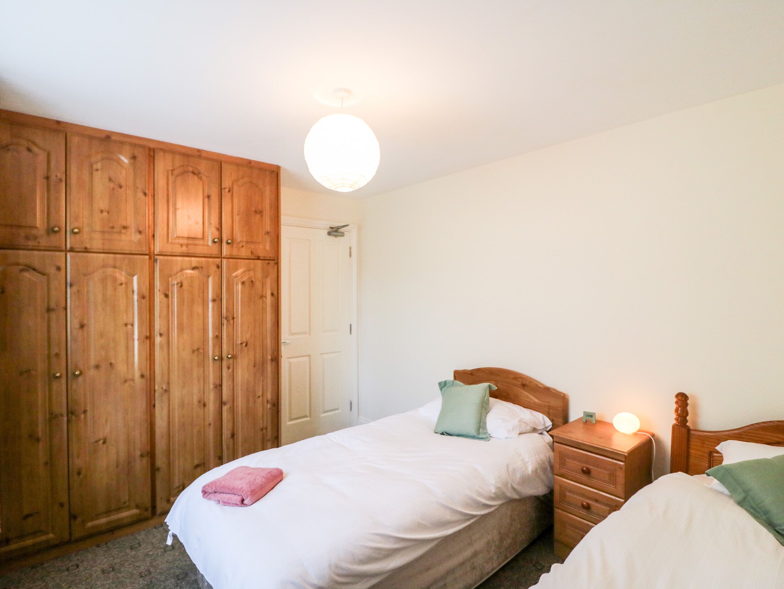 Une chambre à coucher avec une armoire en bois, un lit simple avec un oreiller vert et une table de chevet avec une lampe.