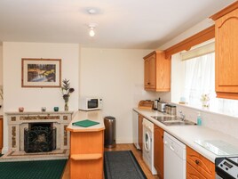 Cocina compacta equipada con microondas, tostadora, fregadero y lavavajillas. Hay una pequeña ventana con cortinas y un cuadro en la pared.