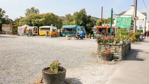 A roadside with food trucks, a sign for Quill's Customer Car Park, and a stone planter with flowers. - 2 Garnish Court (Glengarriff)