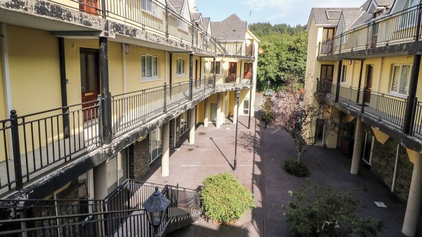 A courtyard with yellow buildings, balconies, and a central pathway. - 2 Garnish Court (Glengarriff)