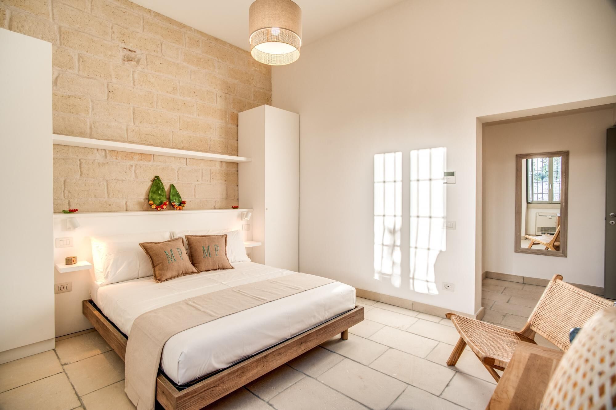 Un dormitorio moderno con pared de ladrillo, cama con estructura de madera, lámpara colgante y ventana con persianas.