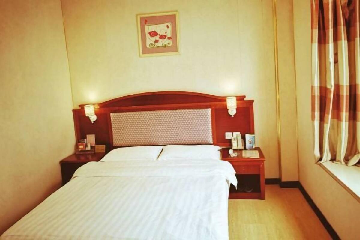 Een hotelkamer met een bed, nachtkastjes, een wandlamp en een raam met gordijnen.