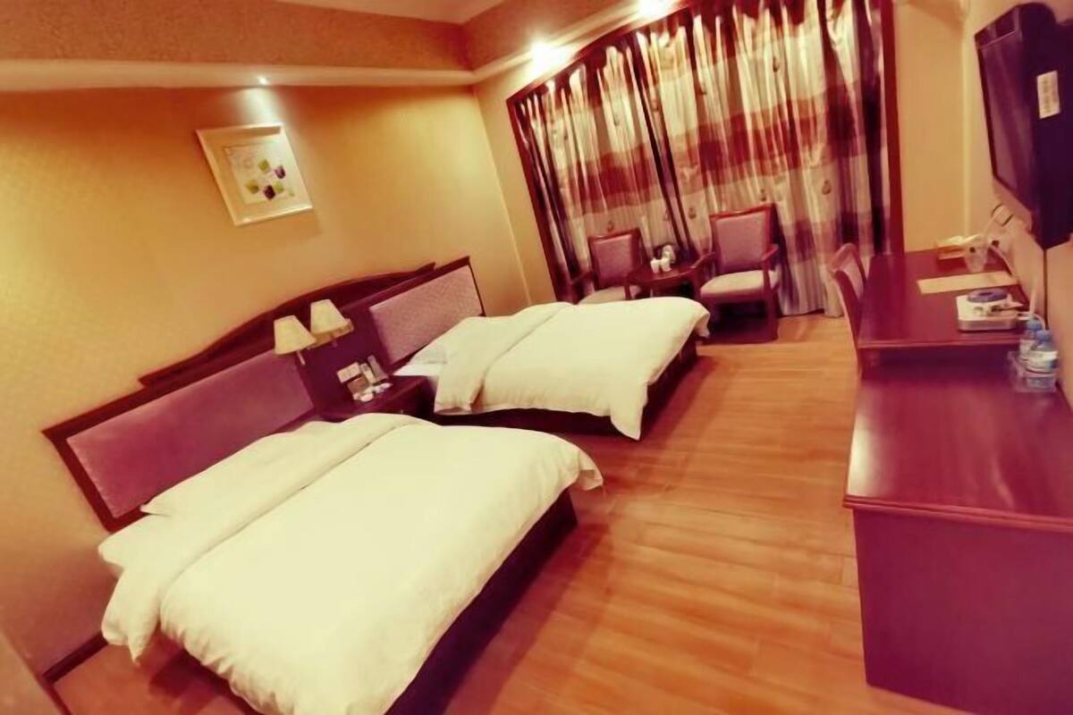Een hotelkamer met twee bedden, een bureau, een stoel, een televisie en een raam met gordijnen.
