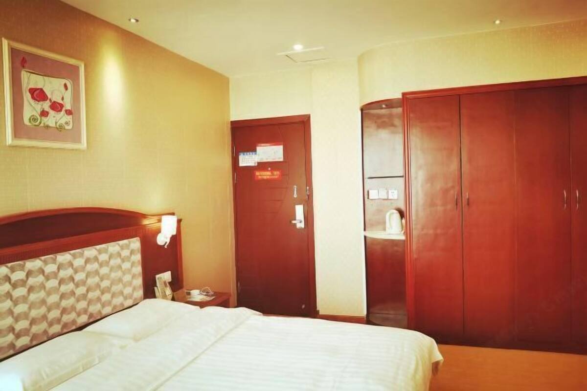 Een hotelkamer met een bed, een houten garderobe, een deur met een bordje en een wandlamp.
