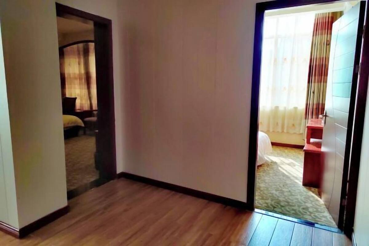 Een hotelkamer met een houten vloer, een bed met een witte spreideken en een raam met gordijnen.