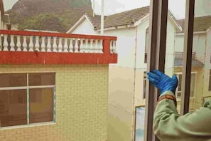 Una persona instalando una ventana en un edificio de ladrillo con un balcón rojo.