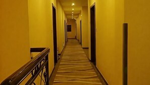 Un couloir d’hôtel avec un sol recouvert de moquette, des portes des deux côtés et une main courante sur le côté gauche.
