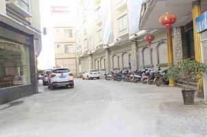 Vista de la calle con coches y motocicletas estacionados, un edificio con una hilera de ventanas y una planta en maceta.