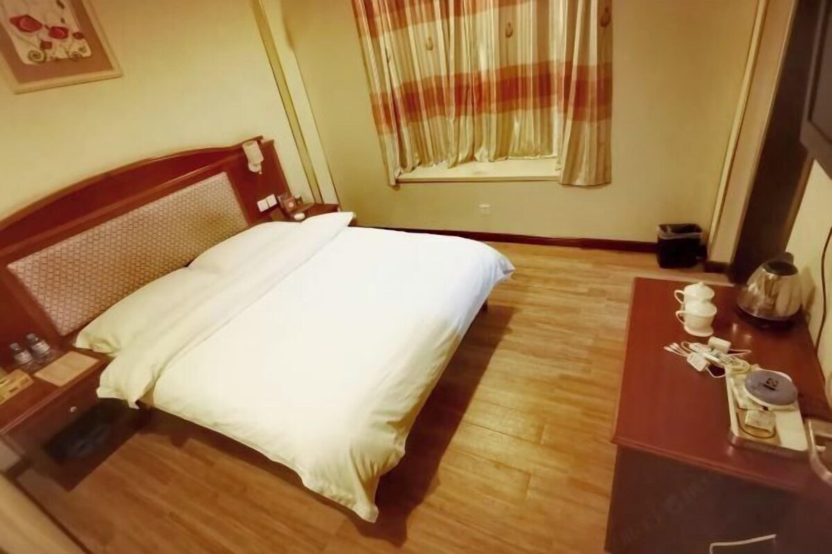 A hotel room with a wooden bed, a bedside table with a cup and saucer, and a window with curtains.