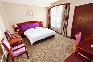 Una habitación de hotel con cama, dos sillas, una mesa, un armario y una ventana con cortinas.
