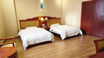 A hotel room with two single beds, a wooden wardrobe, a small table, and a chair.