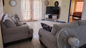 Ein Wohnzimmer mit zwei Sofas, einem Fernseher und einem Standventilator.