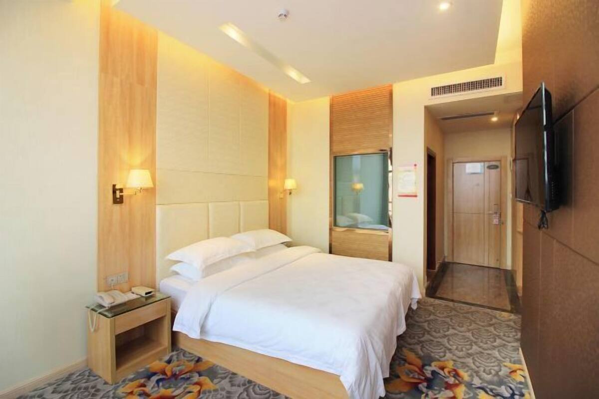 A hotel room with a bed, bedside table, lamp, and a television on the wall.