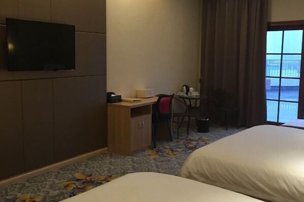 Habitación de hotel con dos camas, un escritorio con una silla, una televisión y una ventana con cortinas.