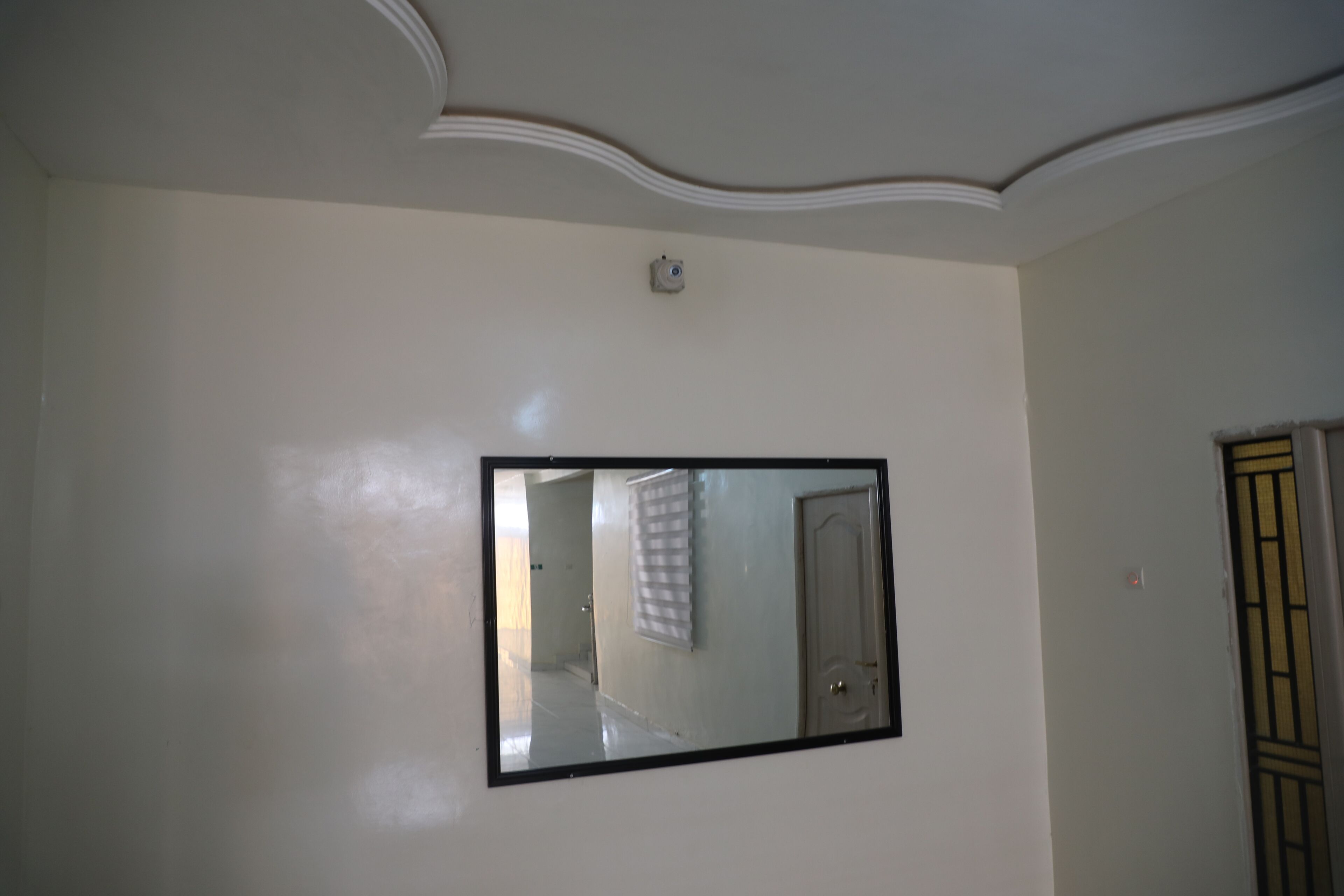 A room with a large mirror on the wall, a door, and a ceiling with a decorative molding.