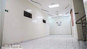 A hallway with white walls, a marble floor, and a staircase on the right. There are signs on the walls and a ceiling light fixture.