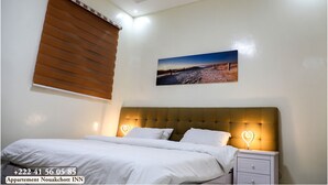 A bedroom with a bed, a nightstand, a wall-mounted picture, and a window with blinds.