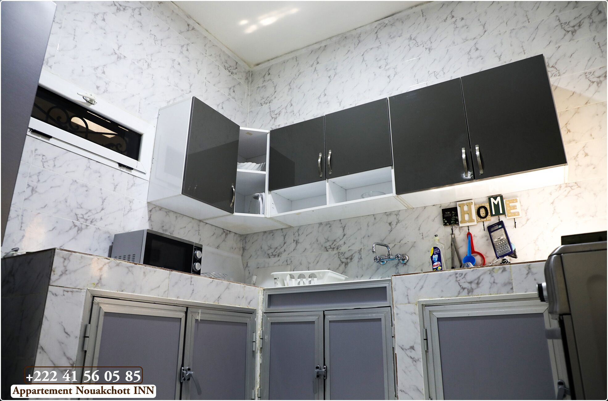 A kitchen with marble walls, black cabinets, and a 'HOME' sign on the wall.