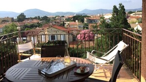 Ein Balkon mit Esstisch, mit Blick auf eine Stadtlandschaft aus Gebäuden und Bergen.