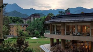 A modern hotel with a curved balcony, lush greenery, and mountains in the background. - Zhonghe Tianyi Hotel (Dujiangyan)