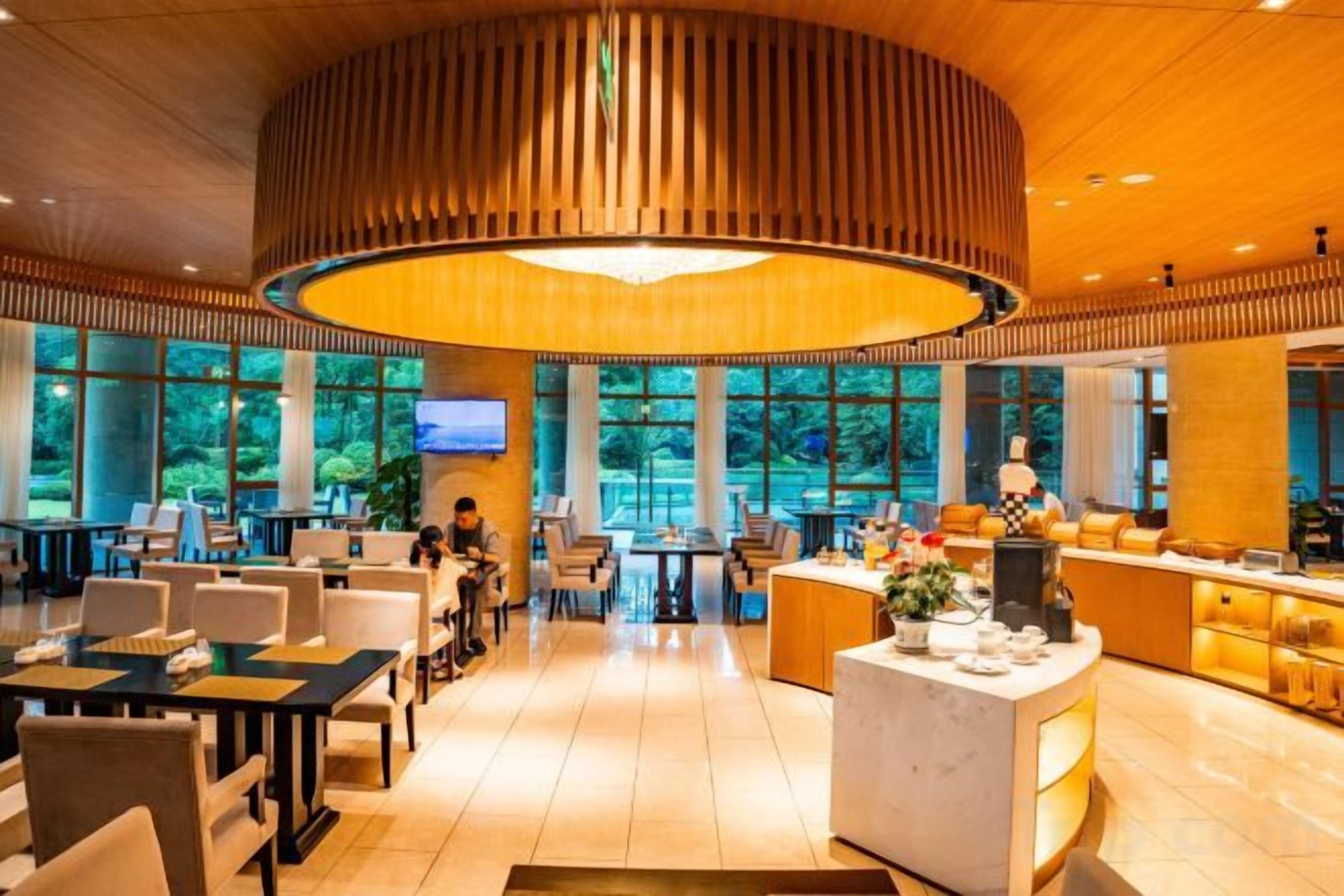 A spacious hotel lobby with a central reception desk, multiple seating areas, and large windows offering a view of the outdoors.