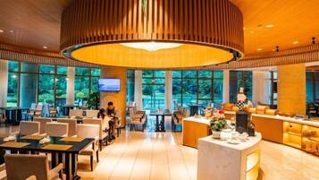 A spacious hotel lobby with a central reception desk, multiple seating areas, and large windows offering a view of the outdoors.