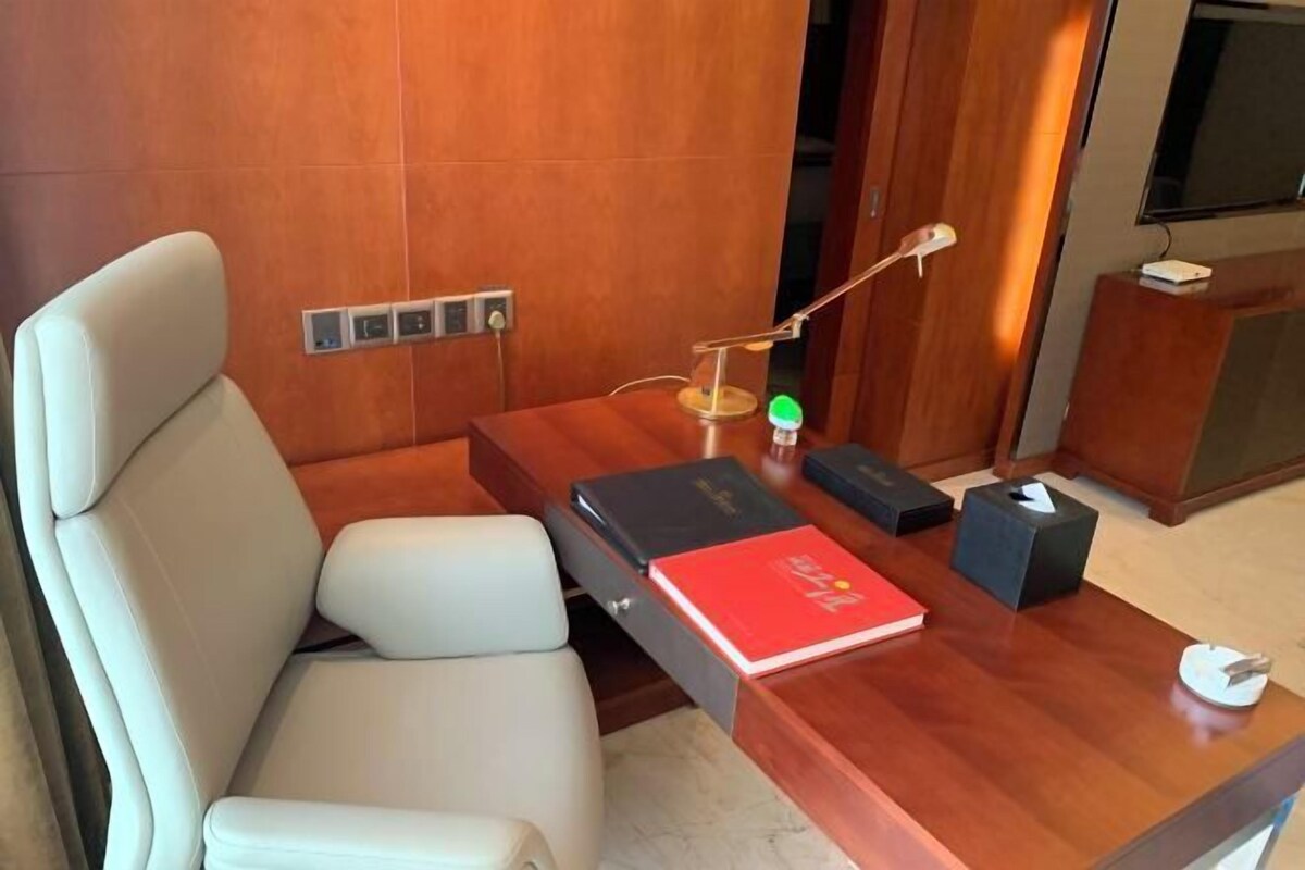 A modern room with a wooden desk, a leather chair, a lamp, and a television.
