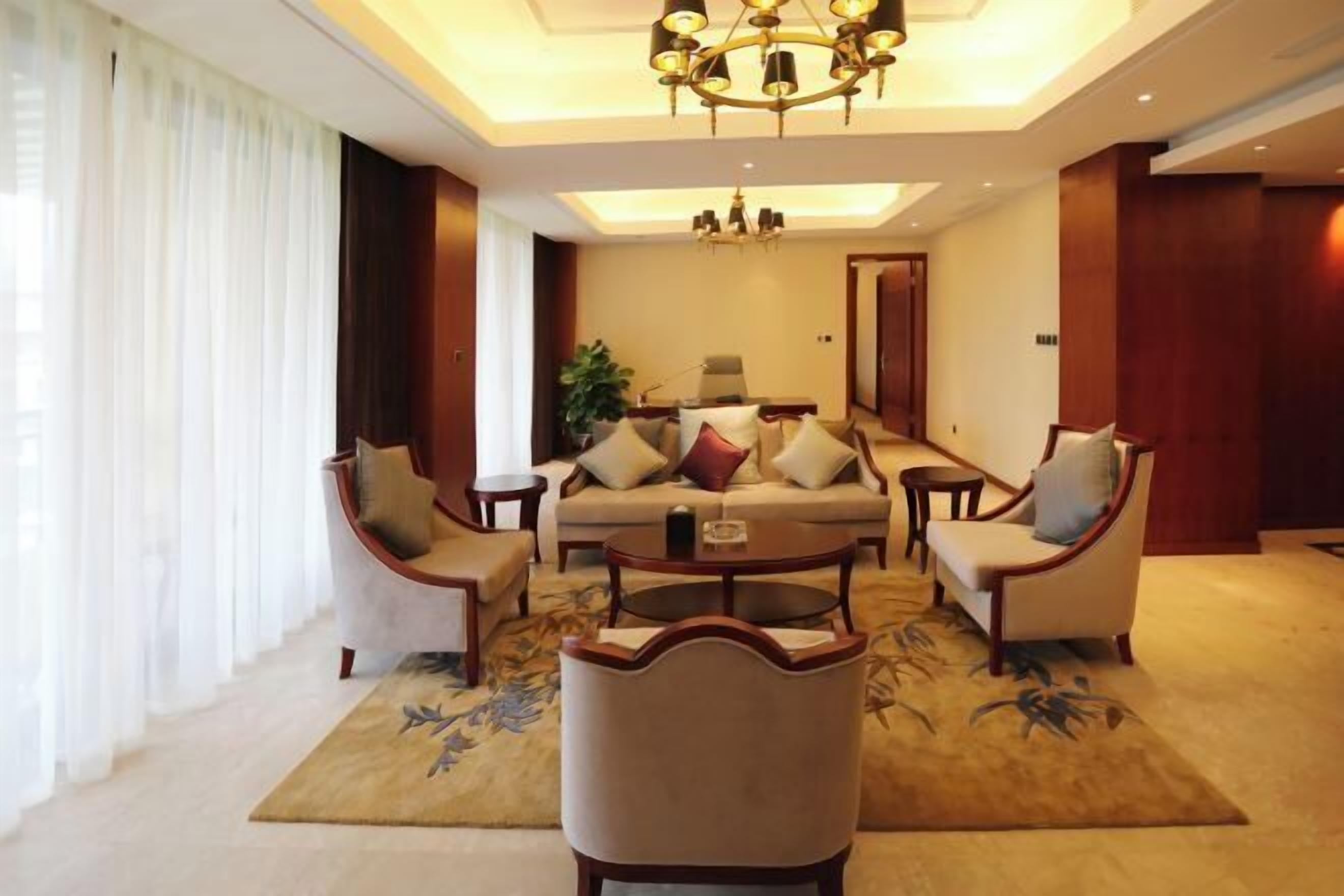 A well-lit living room with a sofa set, two armchairs, a coffee table, and a chandelier.