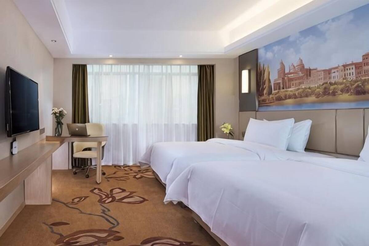 Une chambre d’hôtel avec deux lits, un bureau, une télévision et un tableau au mur.