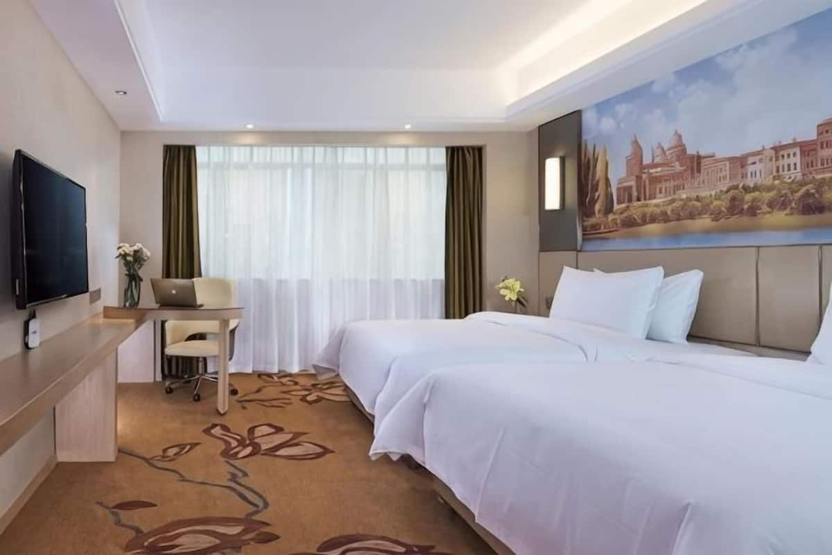 Una habitación de hotel con dos camas, un escritorio, un televisor y un cuadro en la pared.