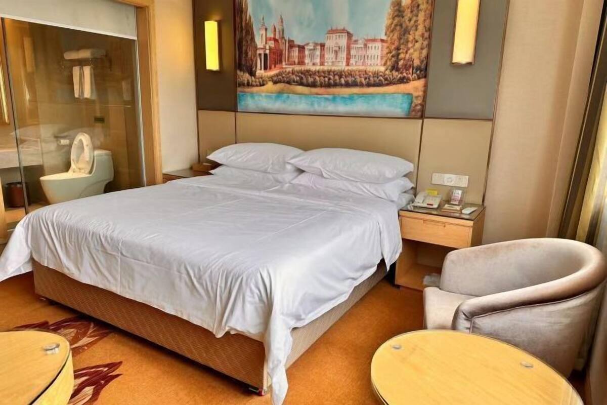 Une chambre d’hôtel avec un lit, une chaise, une petite table, un tableau au mur et une cabine de douche en verre.