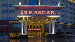 A hotel entrance with a prominent sign, large columns, and a reflective ground. - Vienna International Hotel (Bama) (Bama)