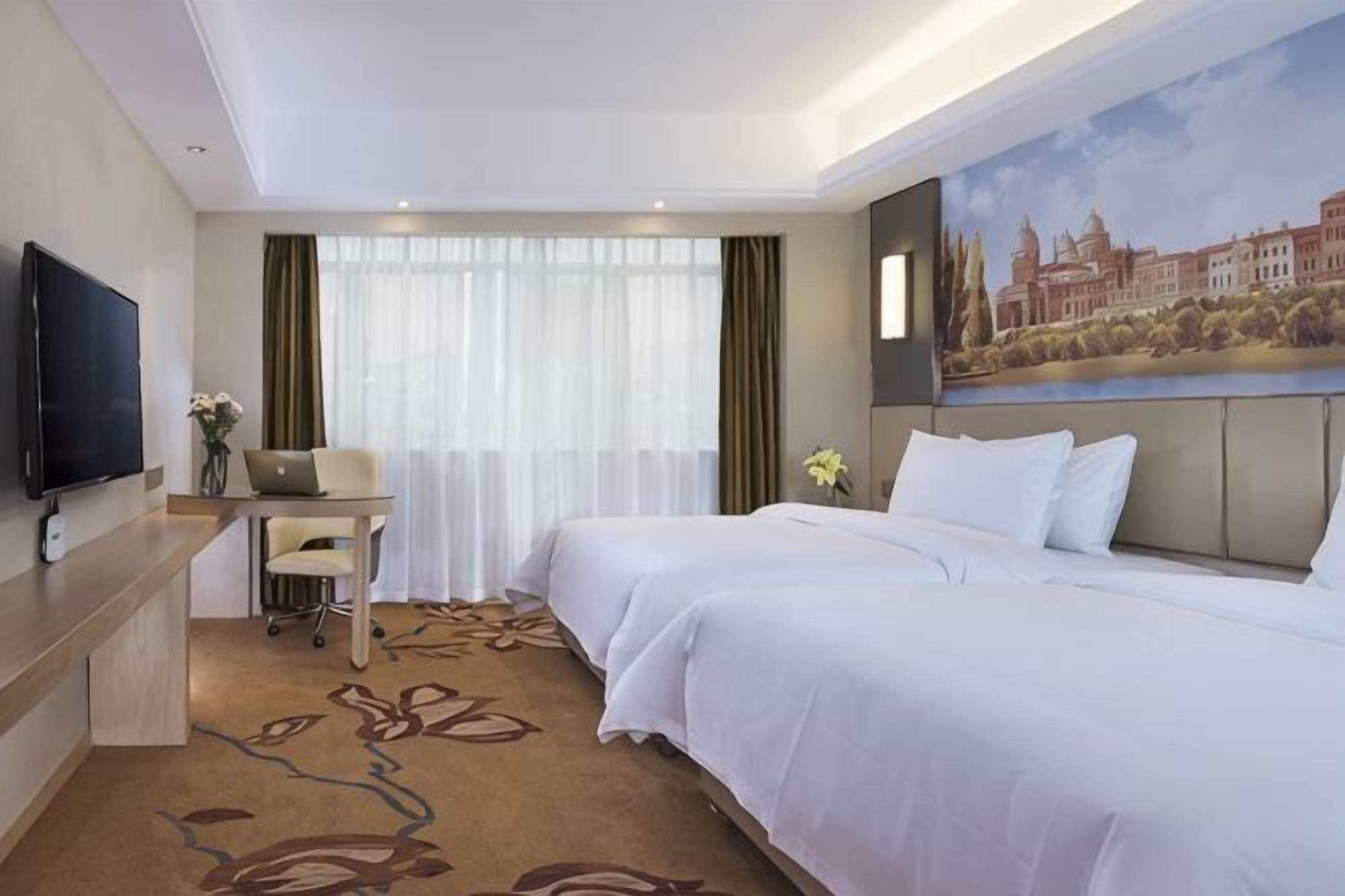 Une chambre d’hôtel avec deux lits, un bureau avec un ordinateur portable, un téléviseur à écran plat et un tableau au mur.