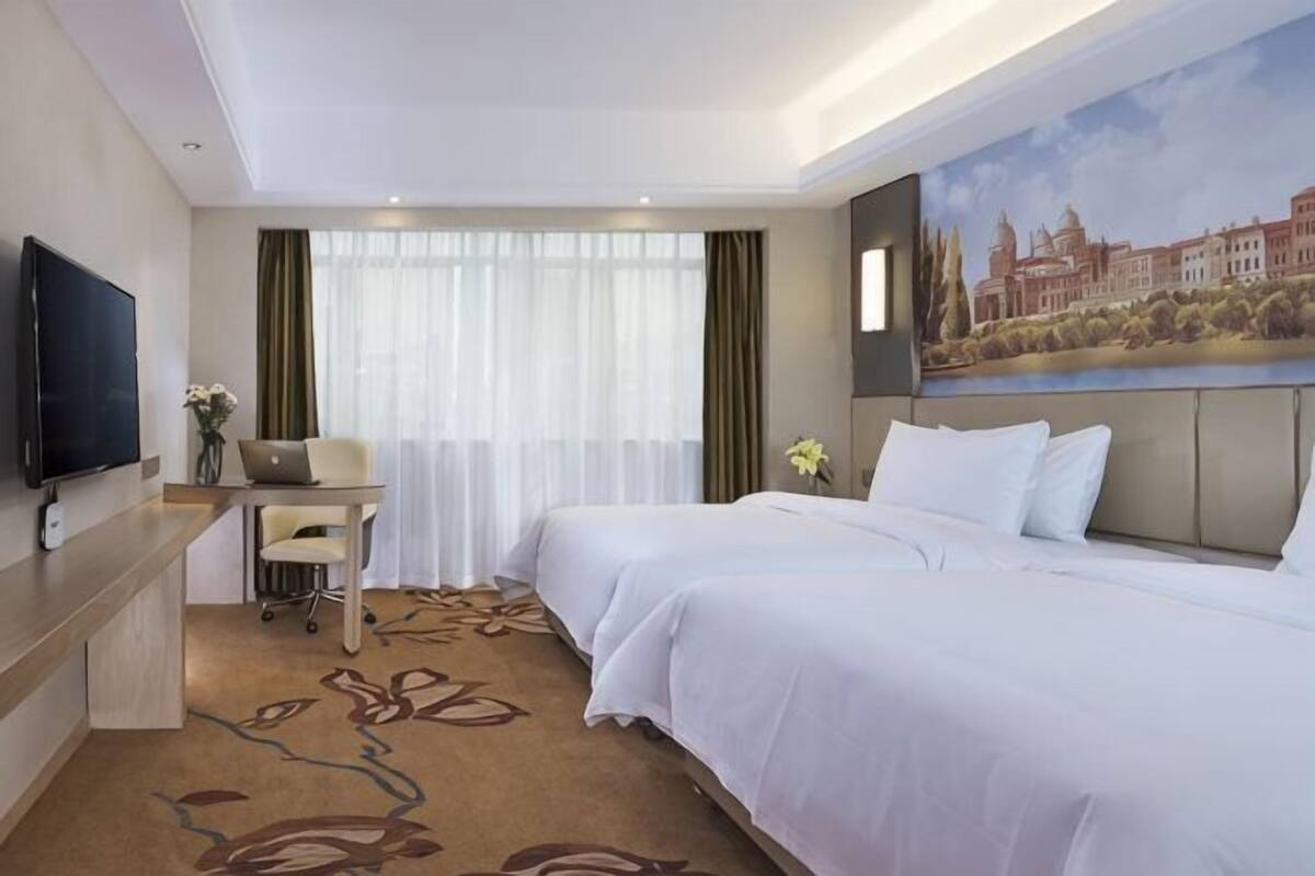 Une chambre d’hôtel avec deux lits, un bureau avec un ordinateur portable, un téléviseur à écran plat et un tableau au mur.