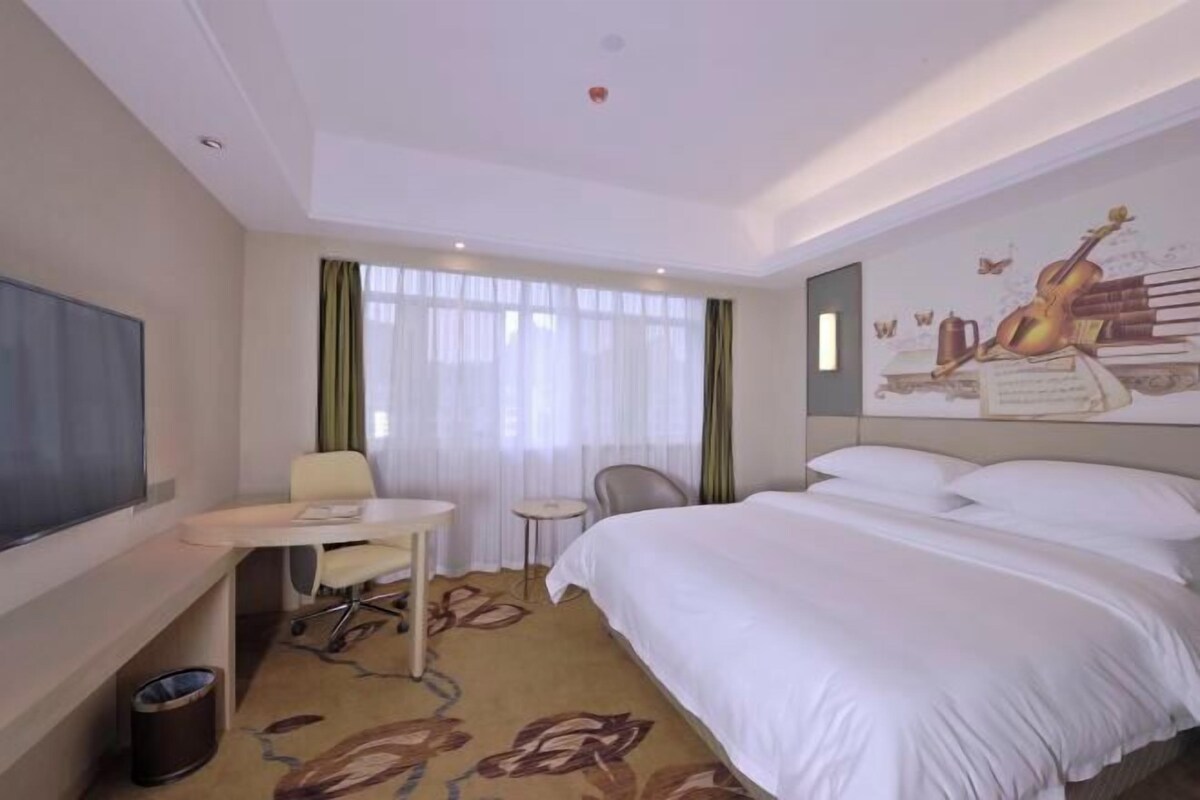 Habitación de hotel con cama, escritorio, silla, televisión y ventana con cortinas.