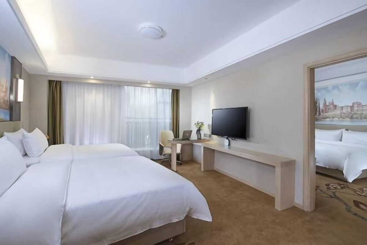 Une chambre d’hôtel avec deux lits, un bureau, une télévision et un tableau représentant un paysage urbain.