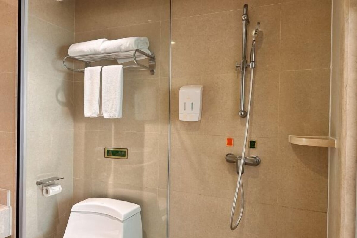 Un baño moderno con cabina de ducha de vidrio, un inodoro, un perchero con dos toallas y un dispensador de jabón.
