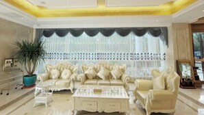A luxurious living room with a cream-colored sofa set, a white coffee table, and a large potted plant. - Vienna International Hotel (Bama) (Bama)