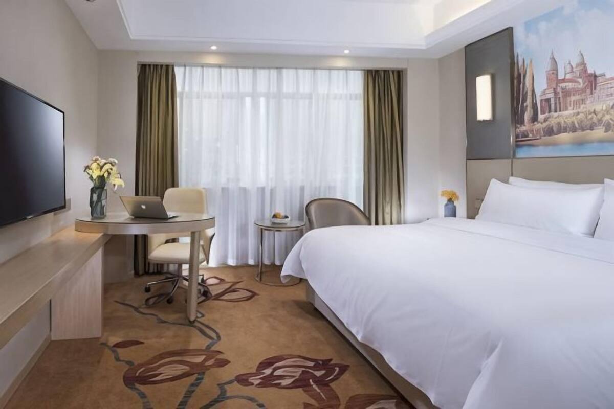 Une chambre d’hôtel avec un lit, un bureau avec un ordinateur portable, une chaise, une télévision et un tableau au mur.