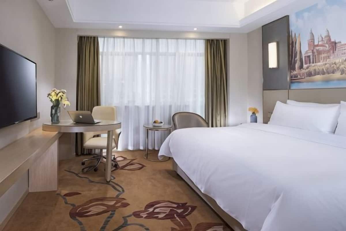 Habitación de hotel con una cama, un escritorio con una computadora portátil, una silla, un televisor y un cuadro en la pared.