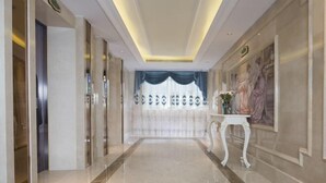 A hallway with a marble floor, a white console table with a vase, and a painting on the wall. - Vienna International Hotel (Bama) (Bama)