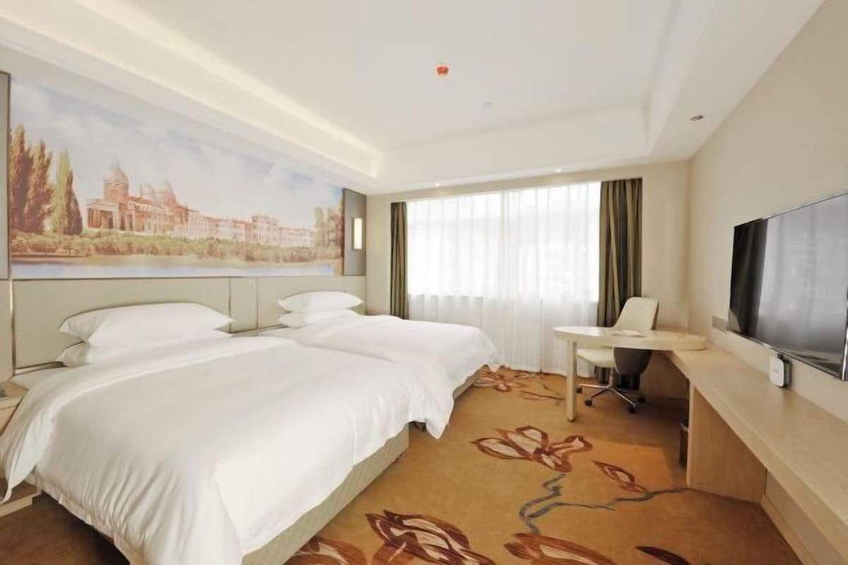Una habitación de hotel con cama, escritorio, silla, televisión y un cuadro en la pared.