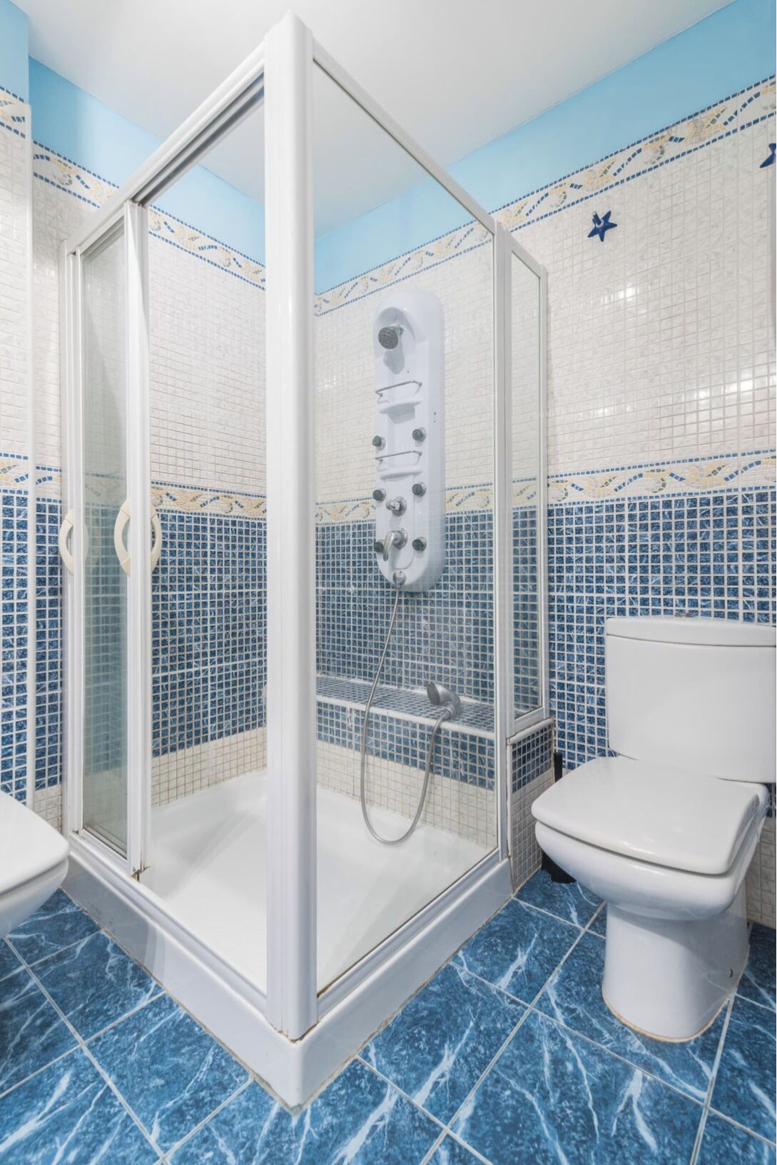 Un baño con ducha de vidrio, inodoro y paredes con azulejos azules.