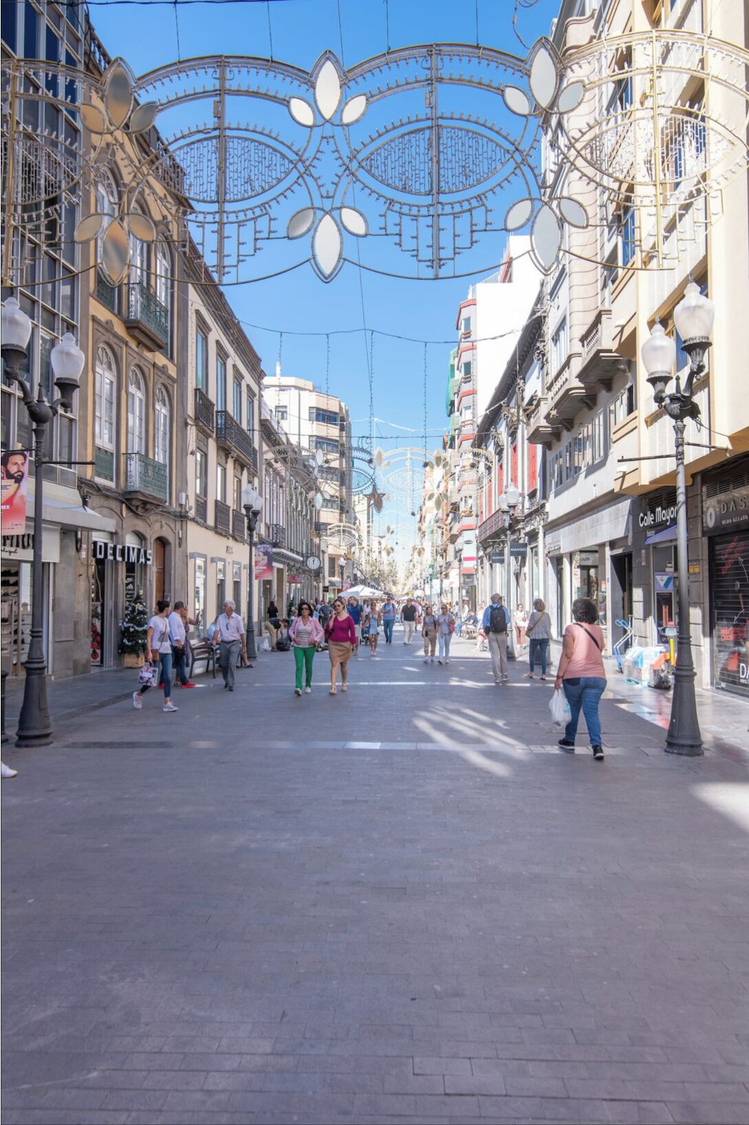 A pedestrian street lined with historic buildings, featuring a clear sky and decorative overhead structures.