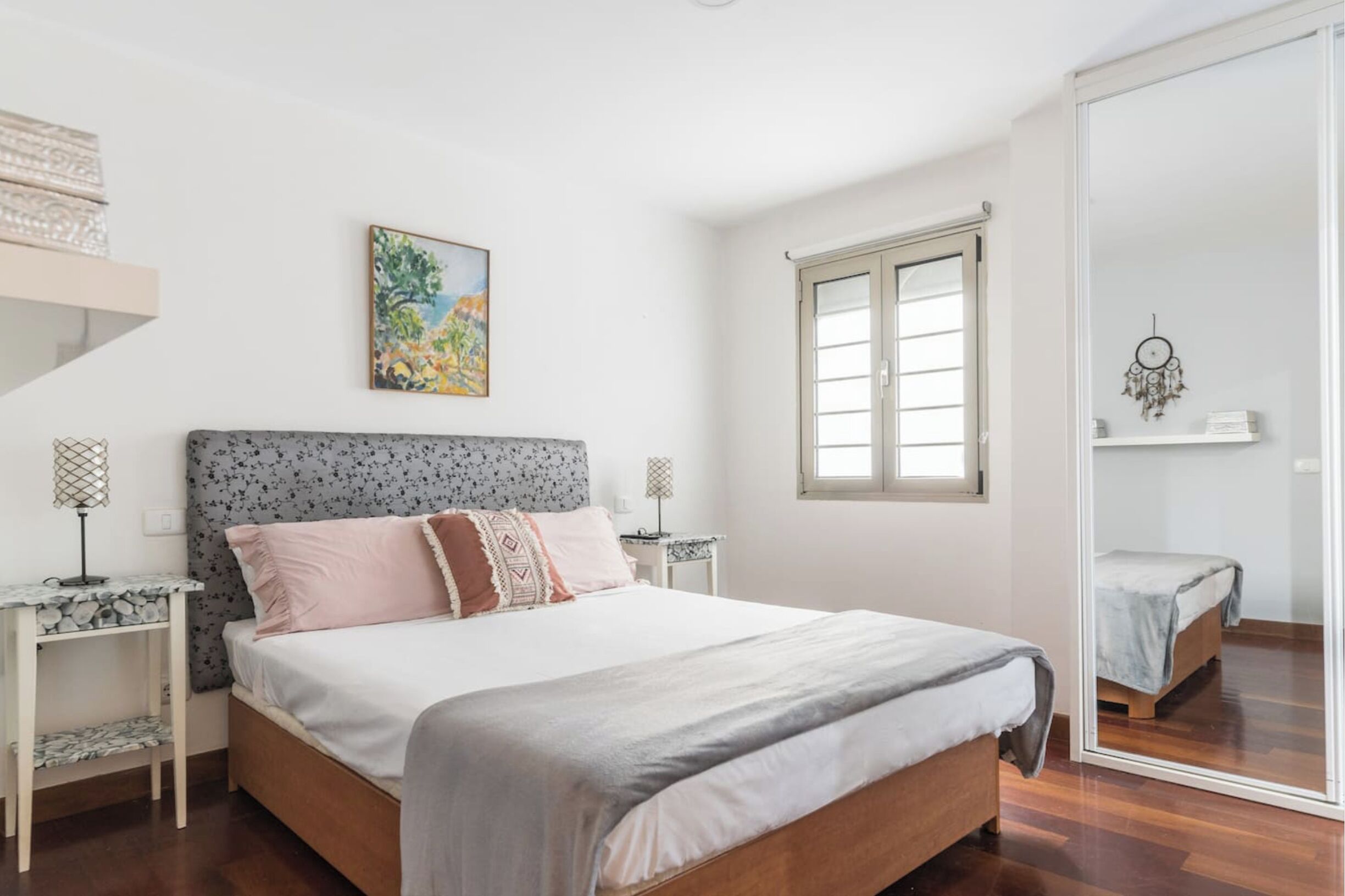 A bedroom with a bed, bedside tables, a window, a painting, and a wardrobe.