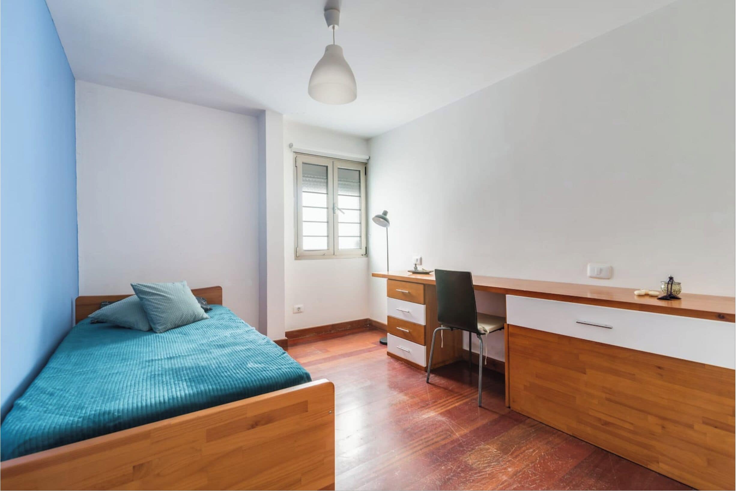 A bedroom with a bed, a desk, and a chair.